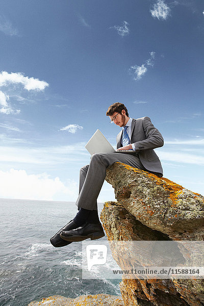 Businessman using laptop on cliff