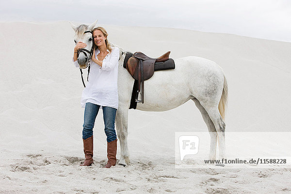Blonde Frau mit Pferd am Strand