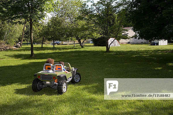 Zwei Kinder fahren Spielzeugauto im Garten