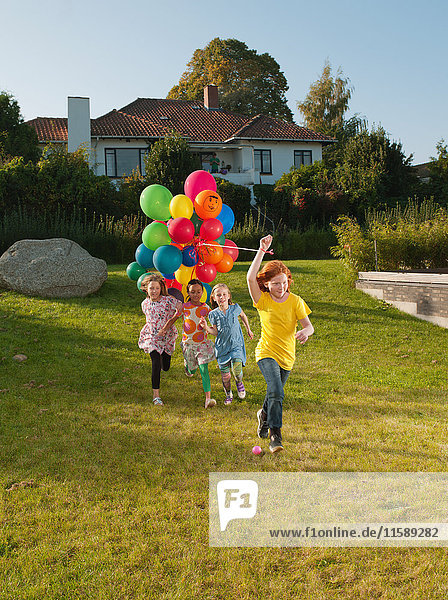 Girls running across lawn with multicoloured balloons