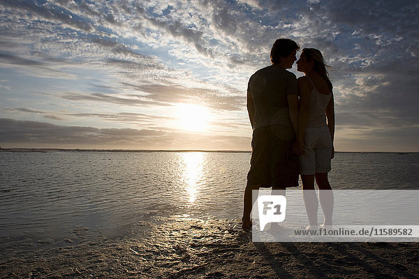 Ein Paar küsst sich bei Sonnenuntergang am Strand