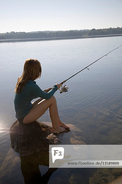 Woman sitting on rock fishing