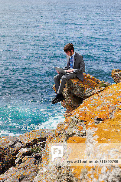 Businessman using laptop on cliff