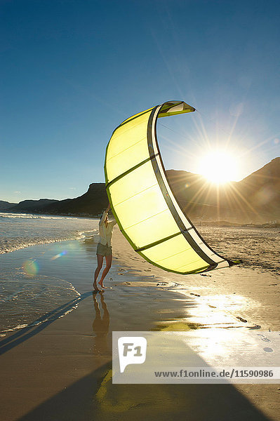 Frau hält Kitesurfing-Segel am Strand.
