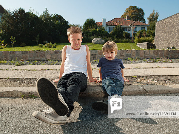 Brothers sitting together on sidewalk