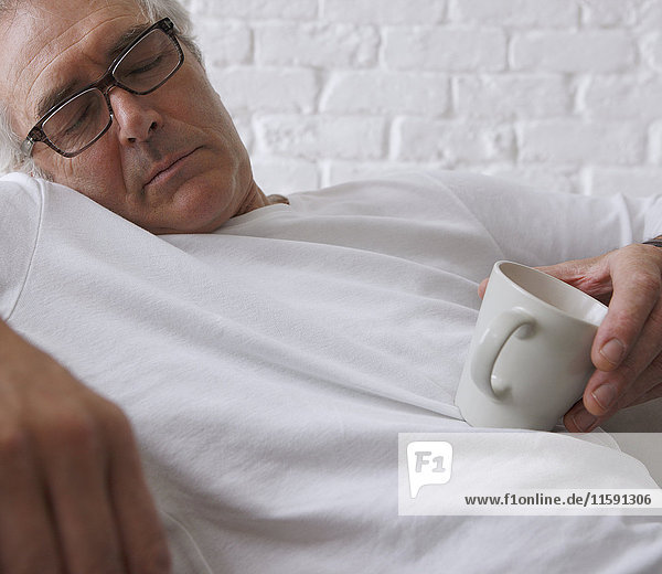 Senior Mann schläft und hält Kaffeetasse
