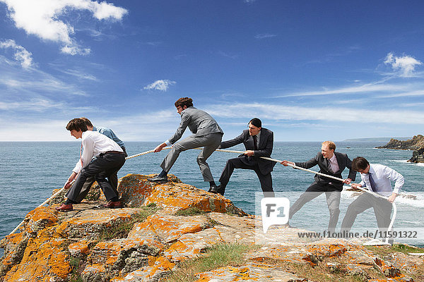 Businessmen pulling rope over cliff