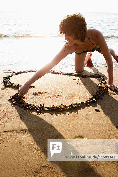 Frau malt Herz im Sand am Strand