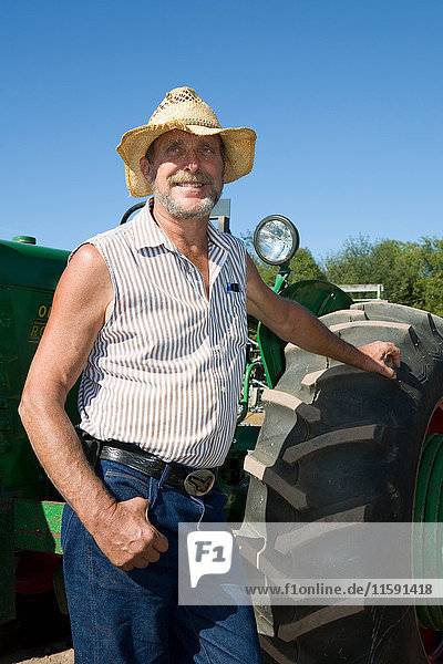 Senior-Landwirt lehnt an Traktor und lächelt