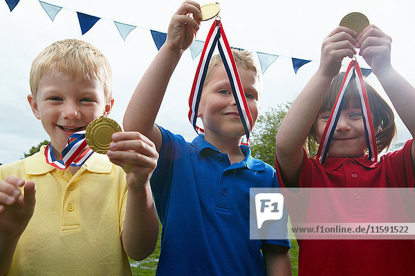 Drei Kinder mit Sportmedaillen auf dem Schulhof