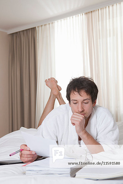 Mann im Bademantel macht Papierkram im Bett