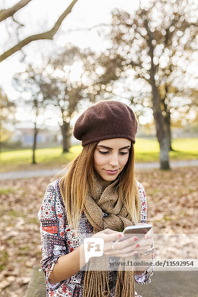 Junge Frau im Herbstpark mit Blick auf das Handy