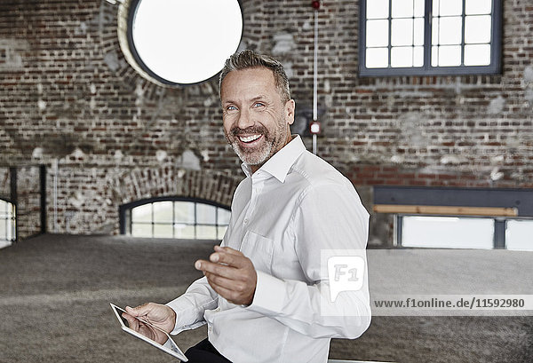 Portrait of happy businessman with tablet in a loft