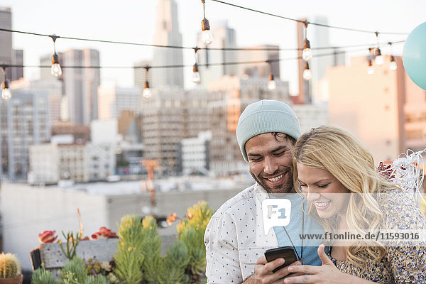 Young couple with balloons standing on rooftop terrace  using smart phone