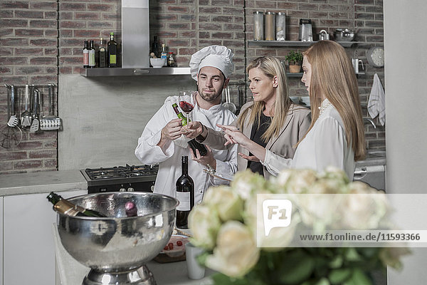 Chefkoch mit zwei Frauen in der Küche bei einer Weinprobe