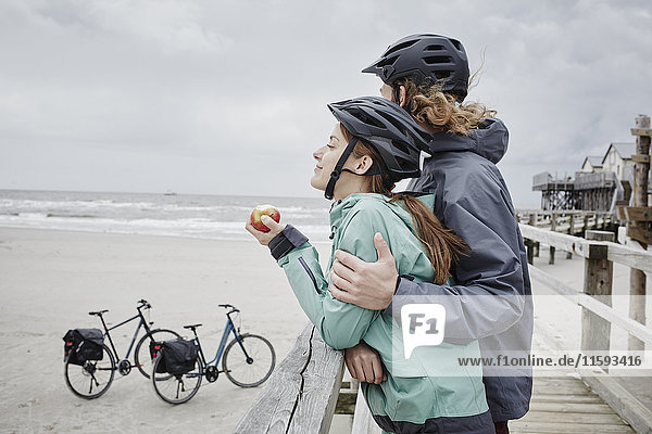 Deutschland  Schleswig-Holstein  St. Peter-Ording  Paar auf einer Fahrradtour mit Pause am Steg am Strand