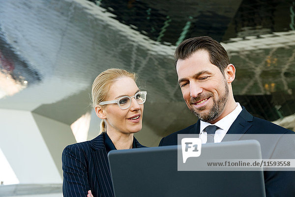 Businessman and businesswoman using laptop outdoors