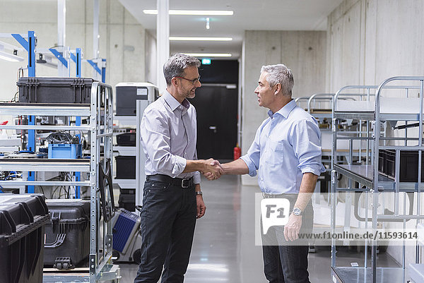 Two businessmen shaking hands in factory hall