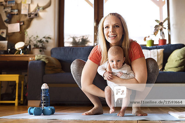 Smiling mother with baby and dumbbells at home