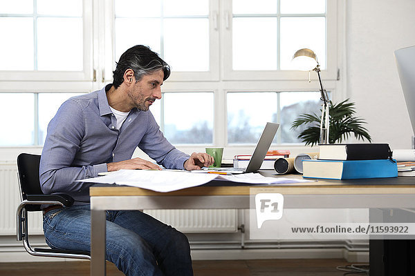 Mann mit Laptop am Schreibtisch im Büro