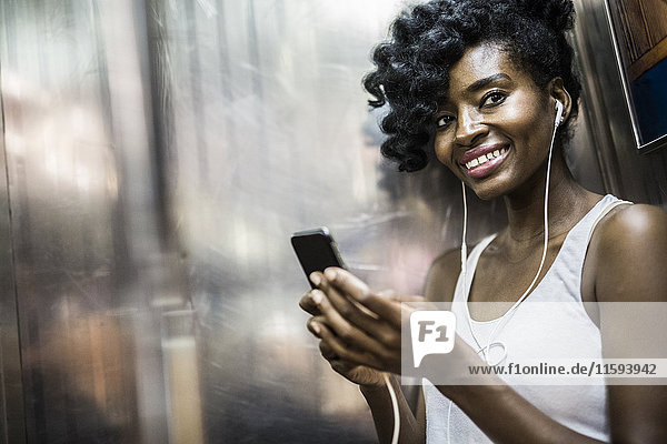 Portrait of happy woman with cell phone and earphones in underground train