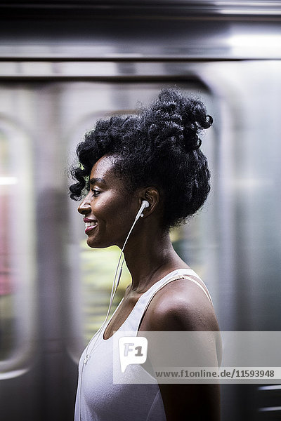 Profil der lächelnden Frau mit Kopfhörern auf dem Bahnsteig der U-Bahn-Station