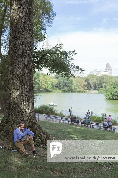 USA  Manhattan  Central Park  man with notebook sitting on a meadow in a park