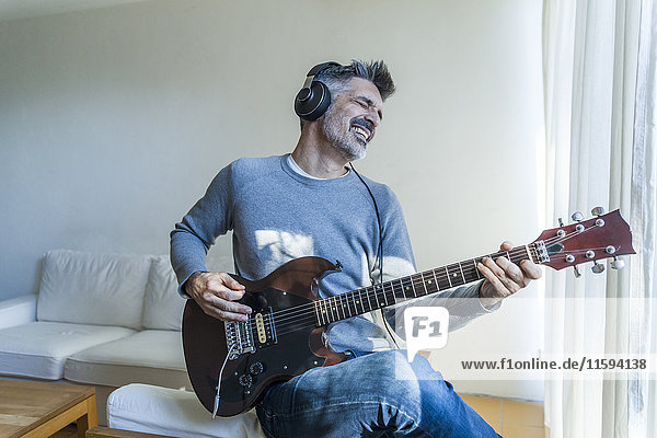Mature man at home playing electric guitar and wearing headphones