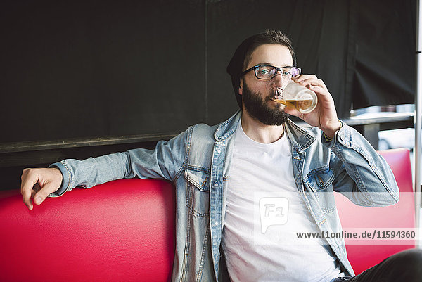 Junger Mann trinkt ein Glas Bier in einer Kneipe.