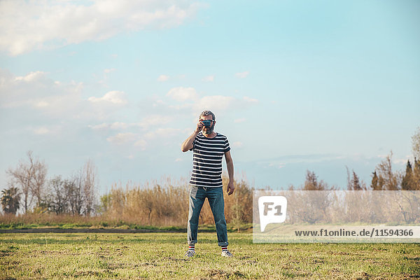 Man standing on a meadow taking photo with vintage camera
