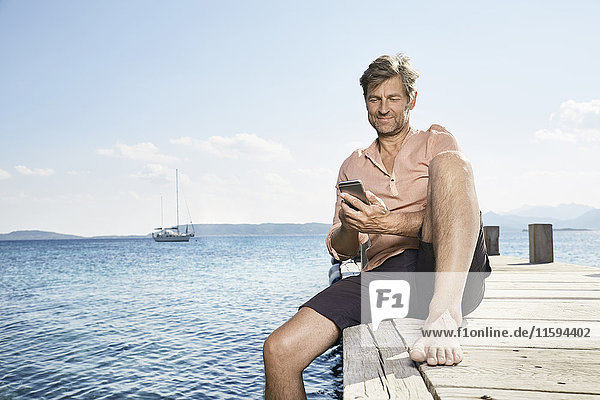 Smiling man sitting on jetty using cell phone