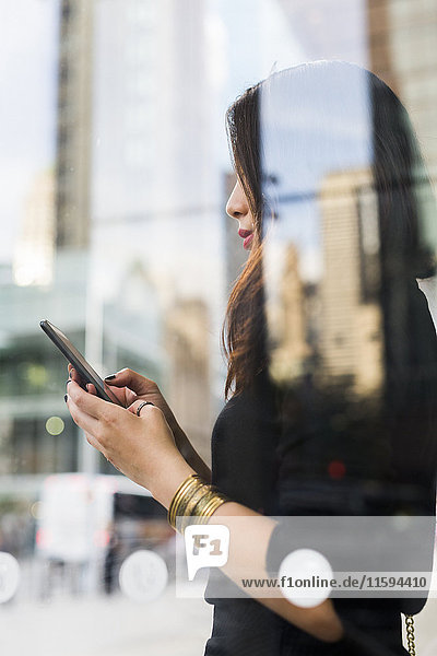 USA  New York City  Manhattan  junge Frau hinter der Glasscheibe beim Blick aufs Handy
