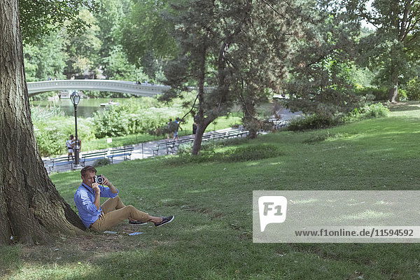 Mann sitzt auf einer Wiese im Park und fotografiert mit der Kamera.