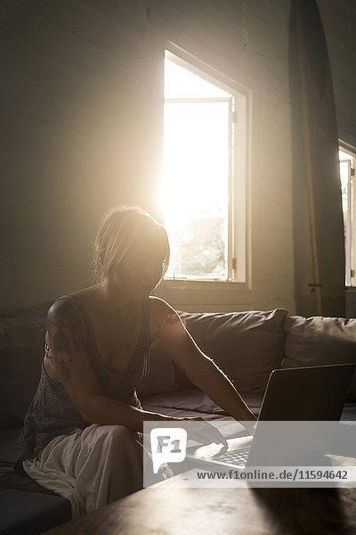 Blond woman sitting on the couch at backlight using laptop
