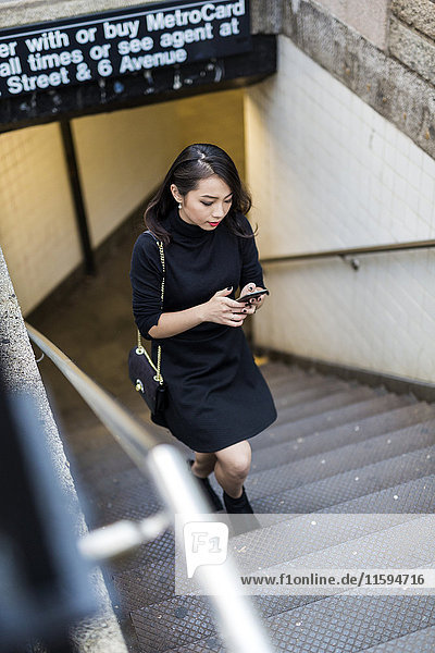 USA  New York City  Manhattan  young woman dressed in black walking upstairs looking at cell phone