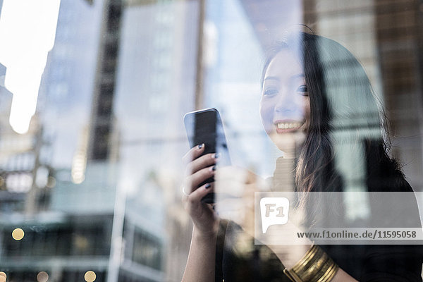 USA  New York City  Manhattan  smiling young woman behind glass pane looking at cell phone