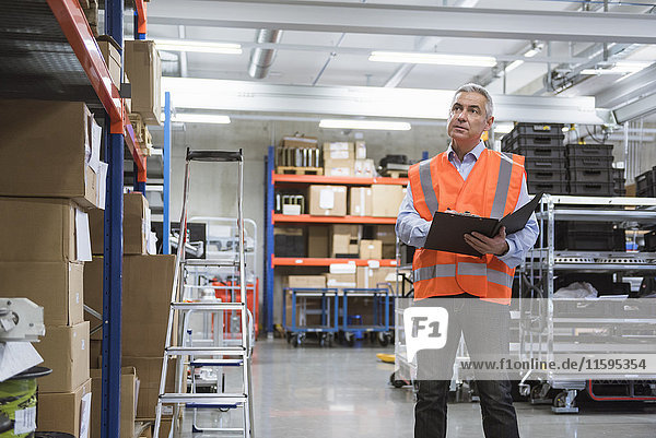 Man in factory hall wearing safety vest holding clipboard