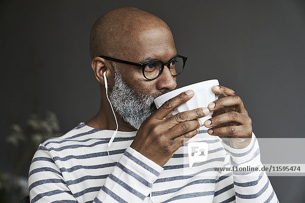 Mature man with earphones drinking coffee