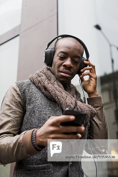 Bald man listening music with headphones looking at cell phone