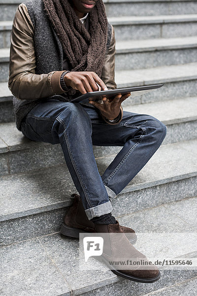 Man sitting on staircase using tablet  partial view