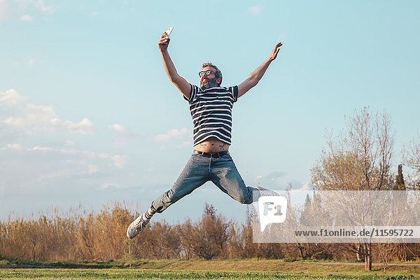Mann springt in die Luft  während er mit dem Smartphone fotografiert.
