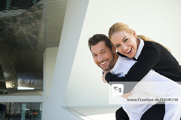 Portrait of happy businessman carrying woman piggyback