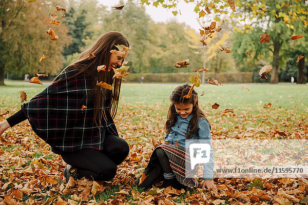 Junge Frau und kleines Mädchen spielen mit Herbstblättern auf einer Wiese