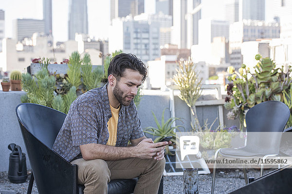 Young man sitting on rooftop terrace checking smart phone messages