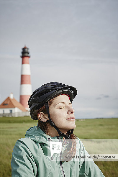 Germany  Schleswig-Holstein  Eiderstedt  woman wearing bicycle helmet relaxing near Westerheversand Lighthouse