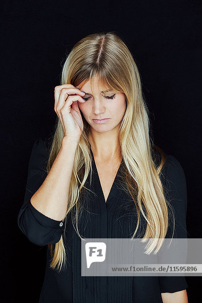Porträt der leidenden blonden Frau vor schwarzem Hintergrund