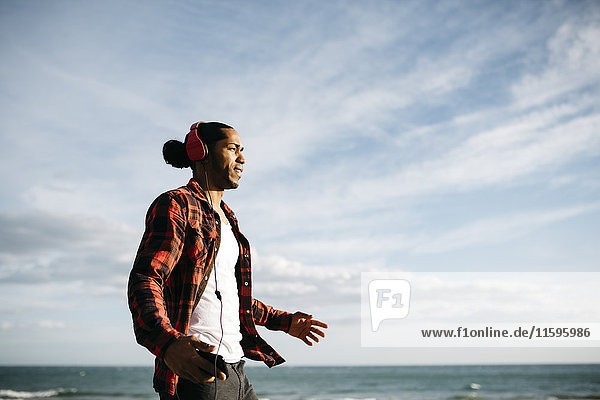 Young man walking in front of the sea listening music with headphones