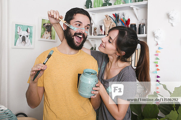 Young woman painting her boyfriend's face with paintbrush