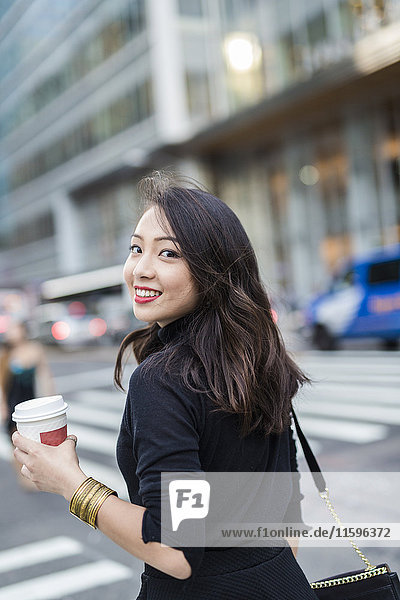 USA  New York City  Manhattan  portrait of smiling young woman with coffee to go crossing the street