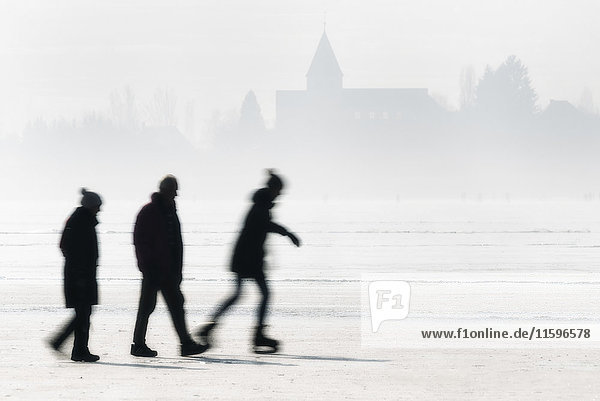 Germany  Lake Constance  Hegne  silhouettes of ice skater and walkers in front of St George's Church at Reichenau